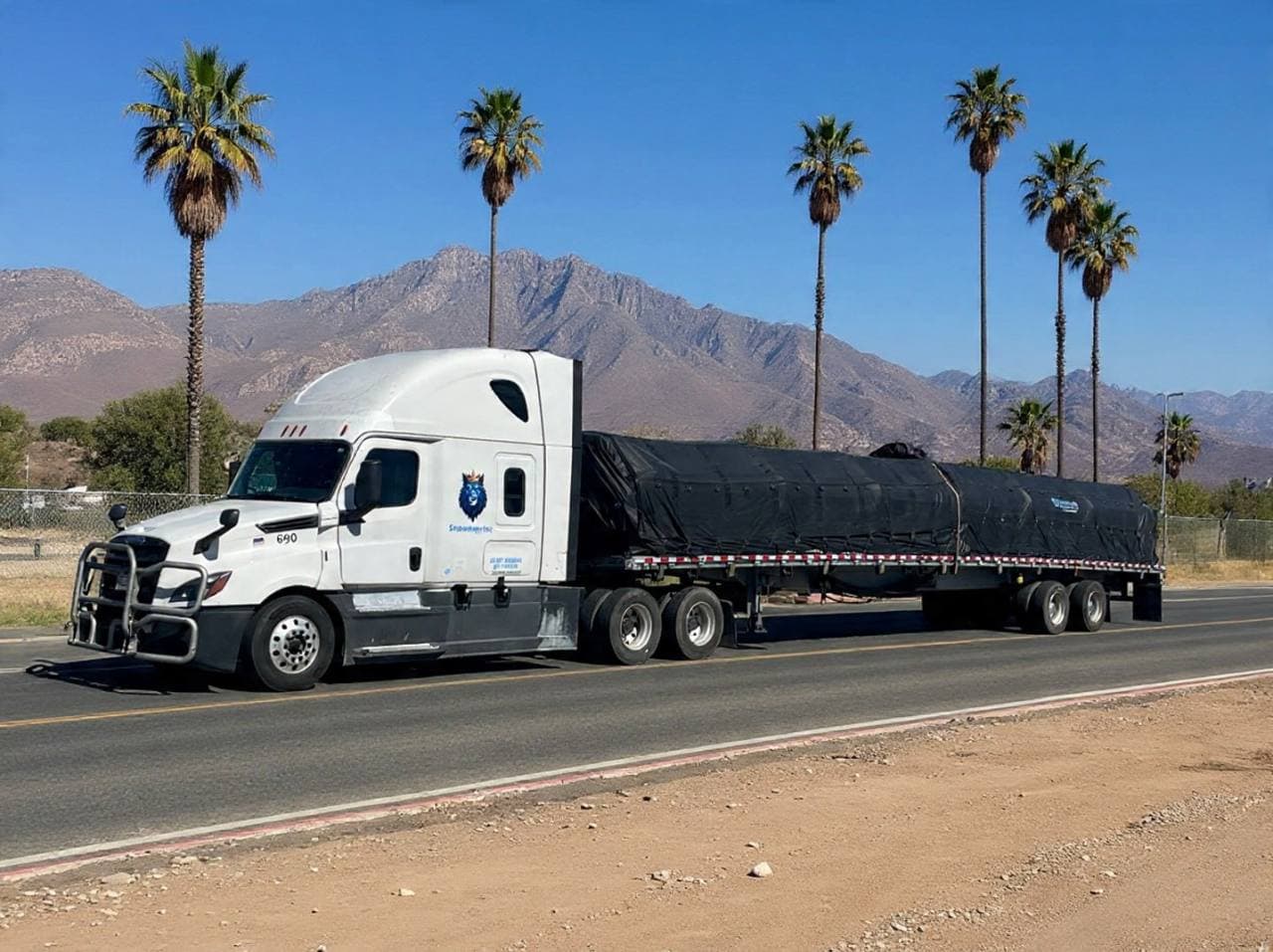 White Snowmen Express truck with covered flatbed load, palm trees and mountains in the background